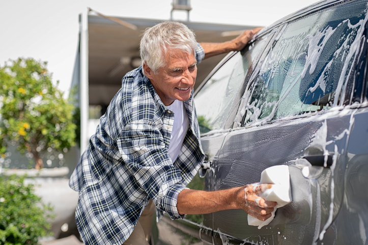 Smiling man washing his car with a sponge.