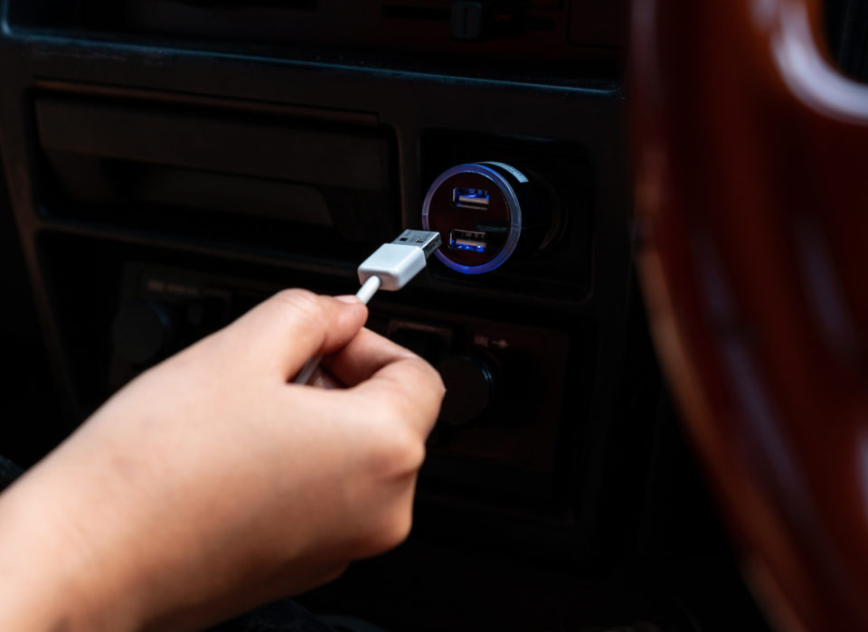 Car interior cabin view of a hand inserting a charging cable into a USB socket