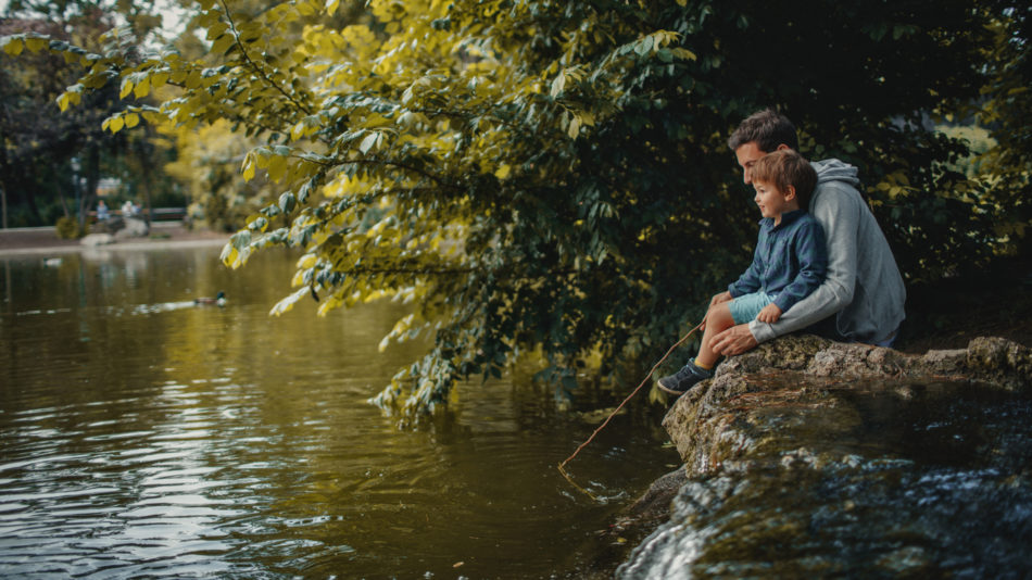 Little smiling boy is learning how to catch a fish in a park pond