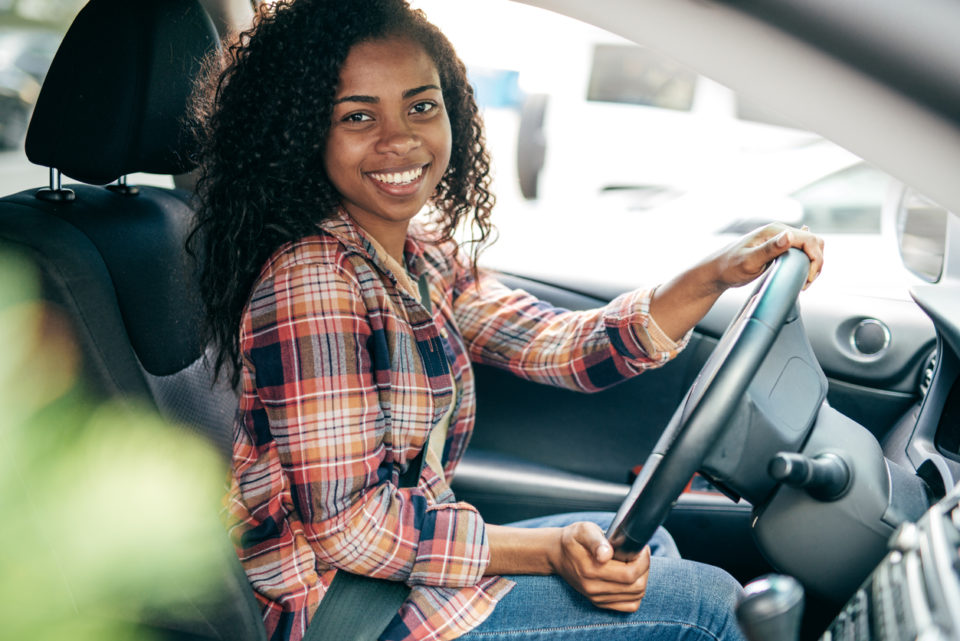 A teenage student driver smiling behind the wheel of a car