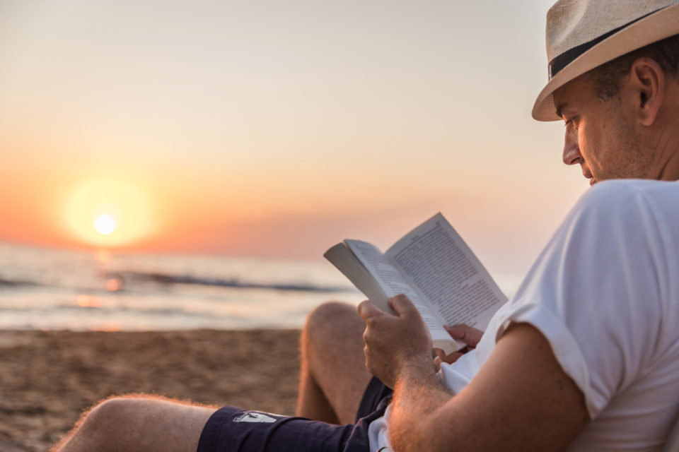 Man reading on a book when sitting on a beach