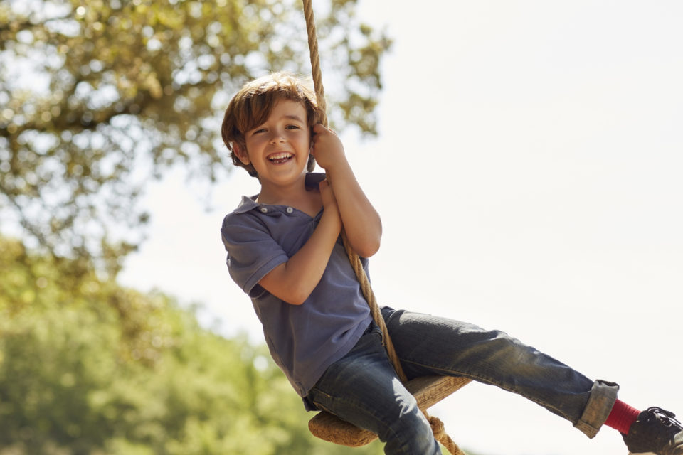 Portrait of cheerful boy playing on swing.