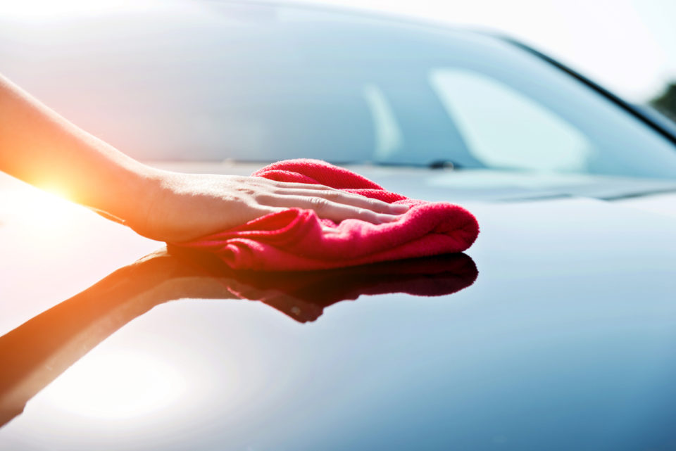 Woman hand drying the vehicle hood with a red towel