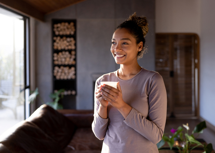 Portrait of a happy African American woman at home warming up her hands with a cup of coffee